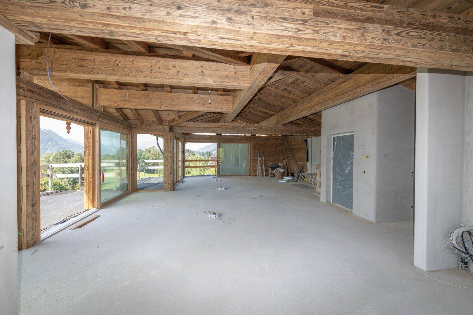 Heller Rohbau mit Holzbalkendecke und großen Fenstern, die Bergblick bieten.