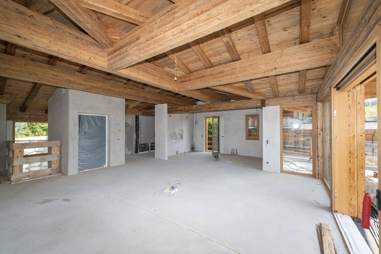 Offener Rohbau mit Holzbalken und großen Fensterfronten für viel Tageslicht.