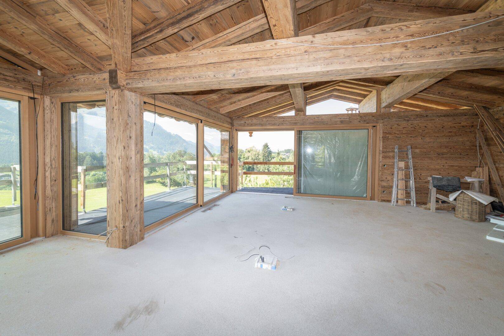 Weitläufiger Rohbau mit Holzbalkendecke und Panoramafenstern zur Berglandschaft.
