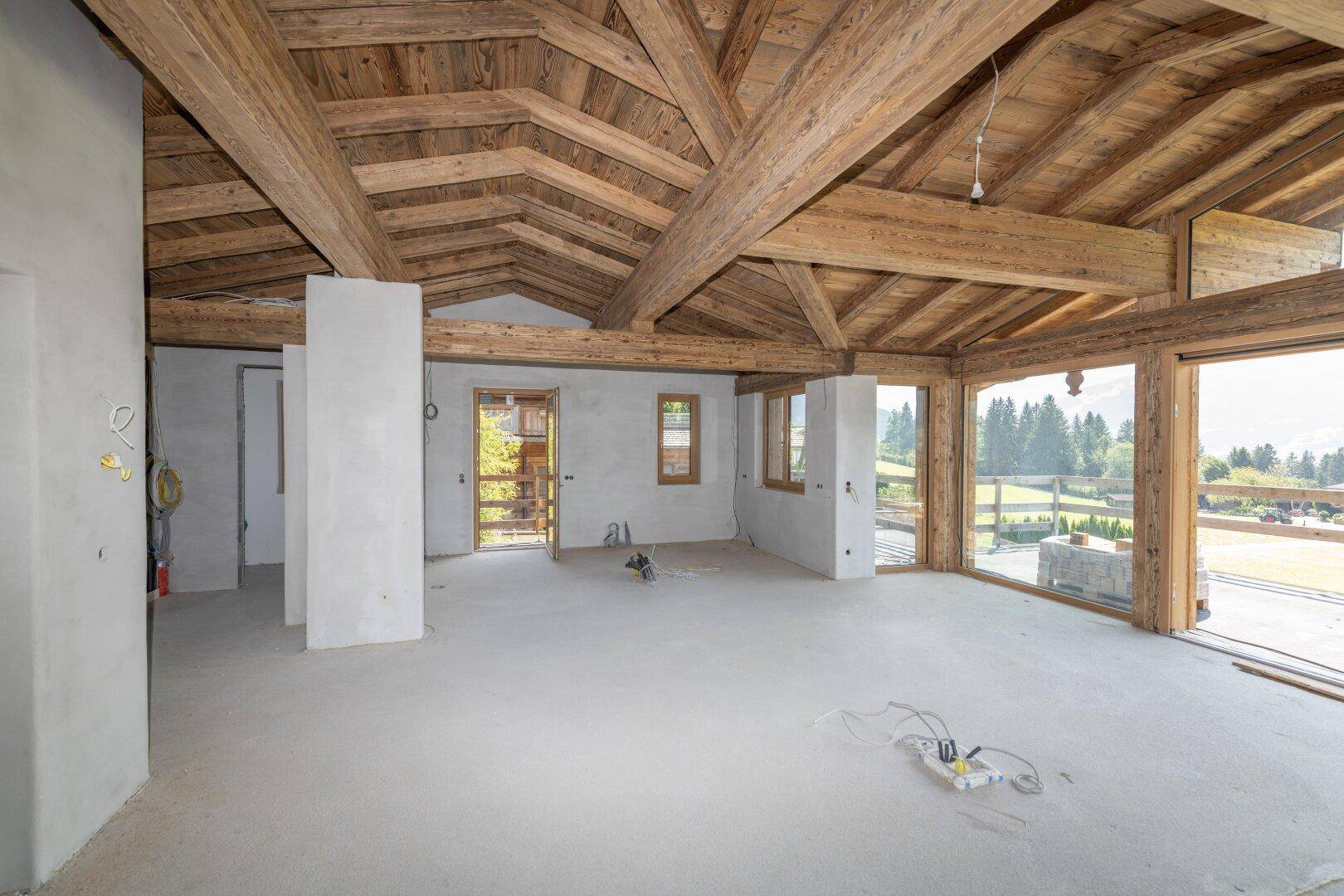 Großer Rohbau mit Holzbalken und vielen Fenstern, die eine helle Atmosphäre schaffen.