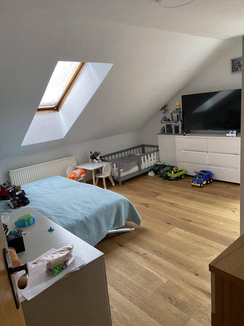 Helles Kinderzimmer im Dachgeschoss mit Holzboden, Dachfenster und Spielzeug.