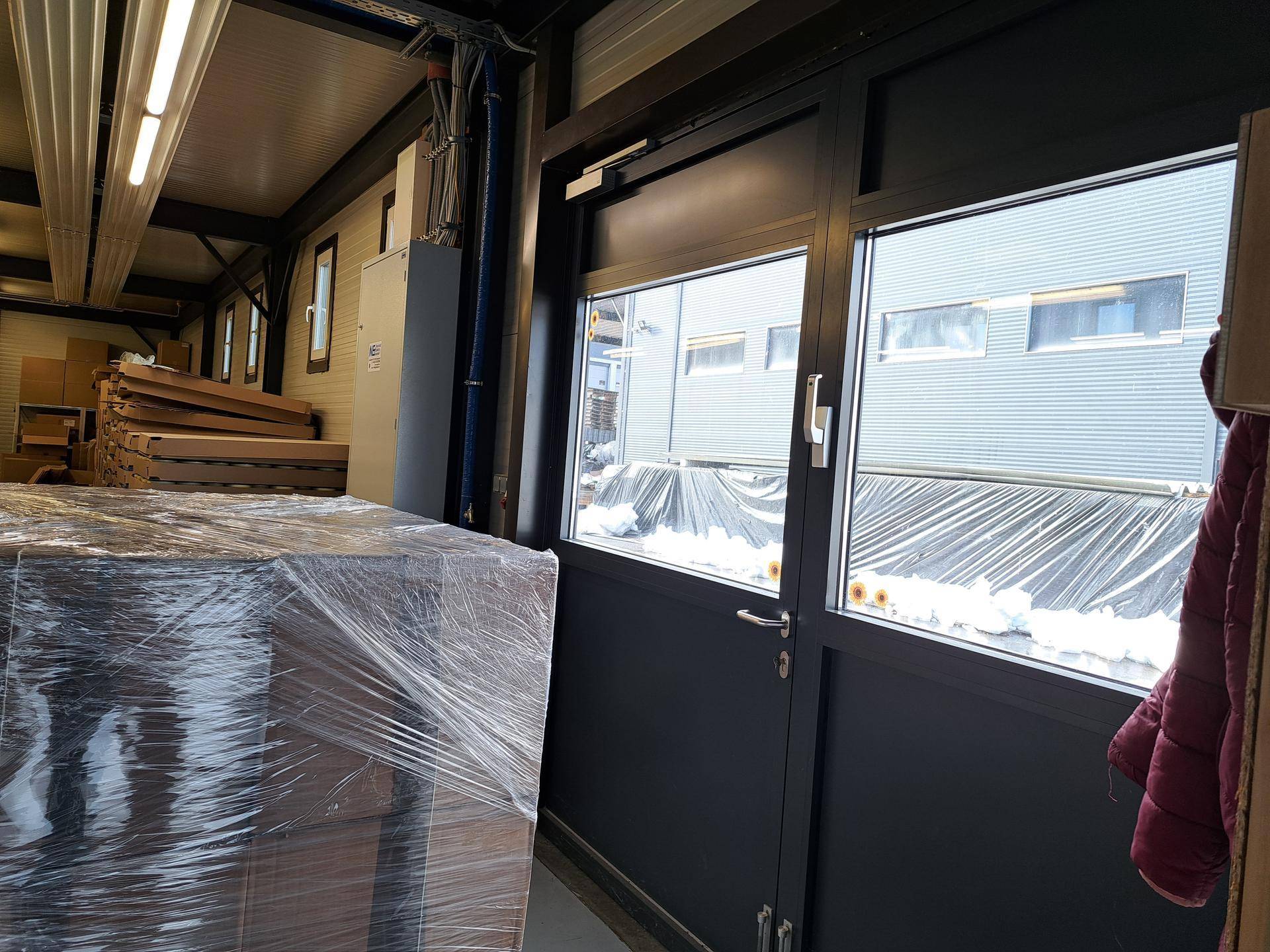 Innenansicht eines Lagerraums mit großen Fenstern und verpackten Paletten, die auf den Transport warten.