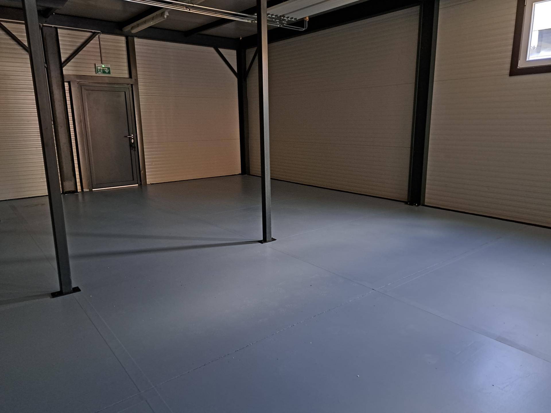 Großer, leerer Lagerraum mit grauem Boden, weißen Wellblechwänden und sichtbaren Stahlträgern.