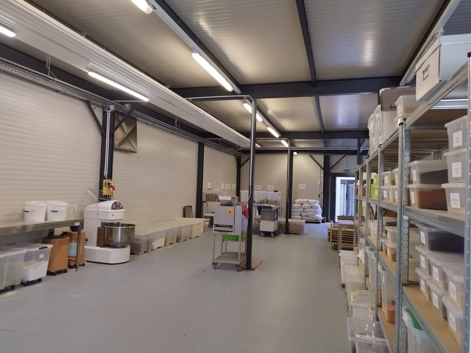 Große Industrieküche oder Produktionsstätte mit verschiedenen Maschinen, Regalen und offenem Deckenbereich.