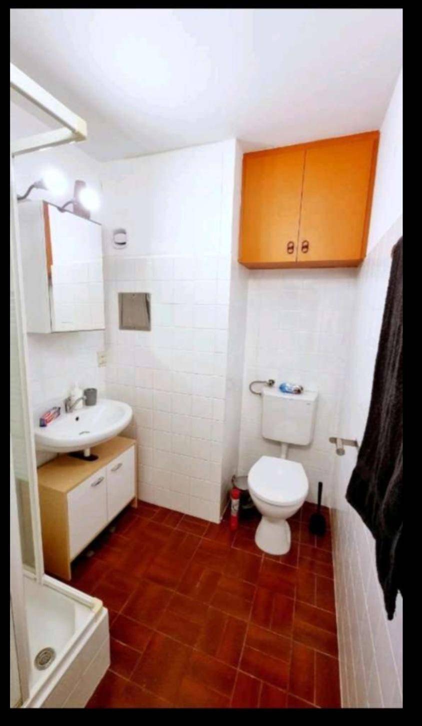 Kompaktes Badezimmer mit WC, Waschbecken, Duschkabine und orangefarbenem Wandschrank.
