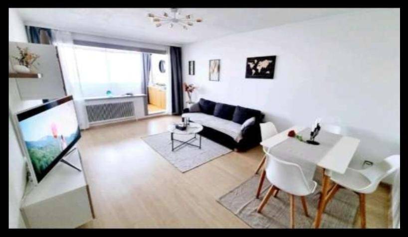 Geräumiger Wohn- und Essbereich mit hellem Laminatboden, bequemer Couch und Zugang zum Balkon.