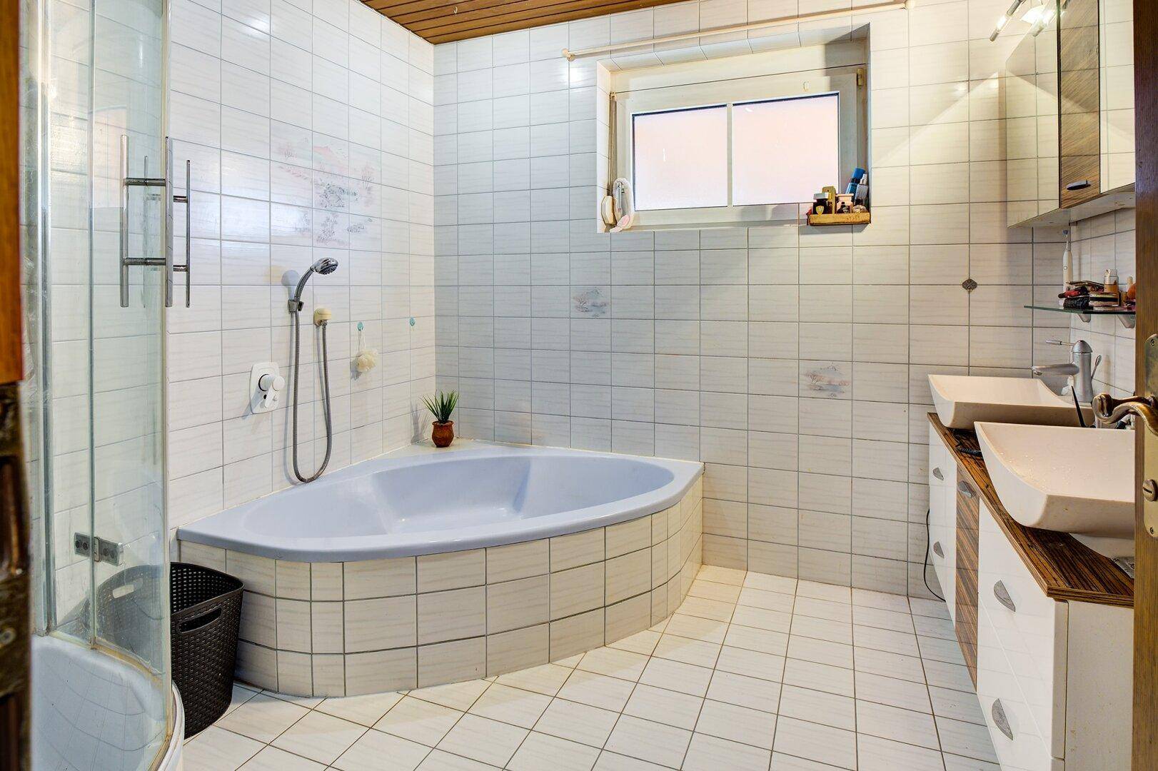 Gefliestes Badezimmer mit Eckbadewanne, Dusche und Doppelwaschbecken, funktional und hell.