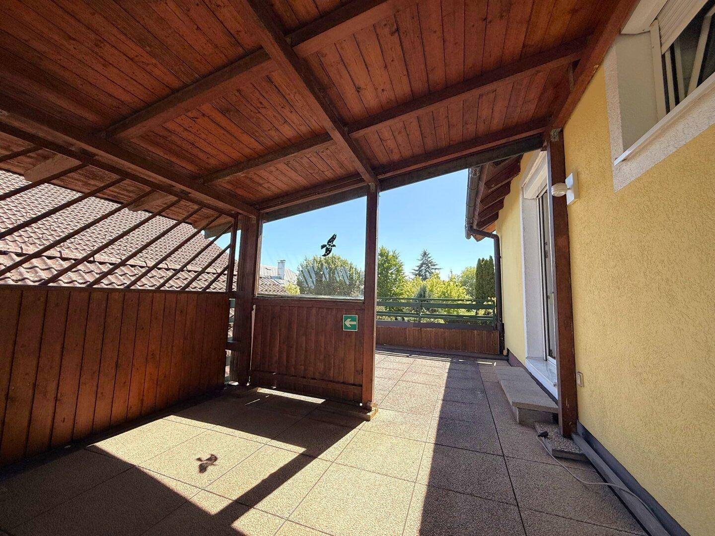 Überdachter Balkon mit Holzboden und Geländer, bietet einen geschützten Außenbereich mit Weitblick.