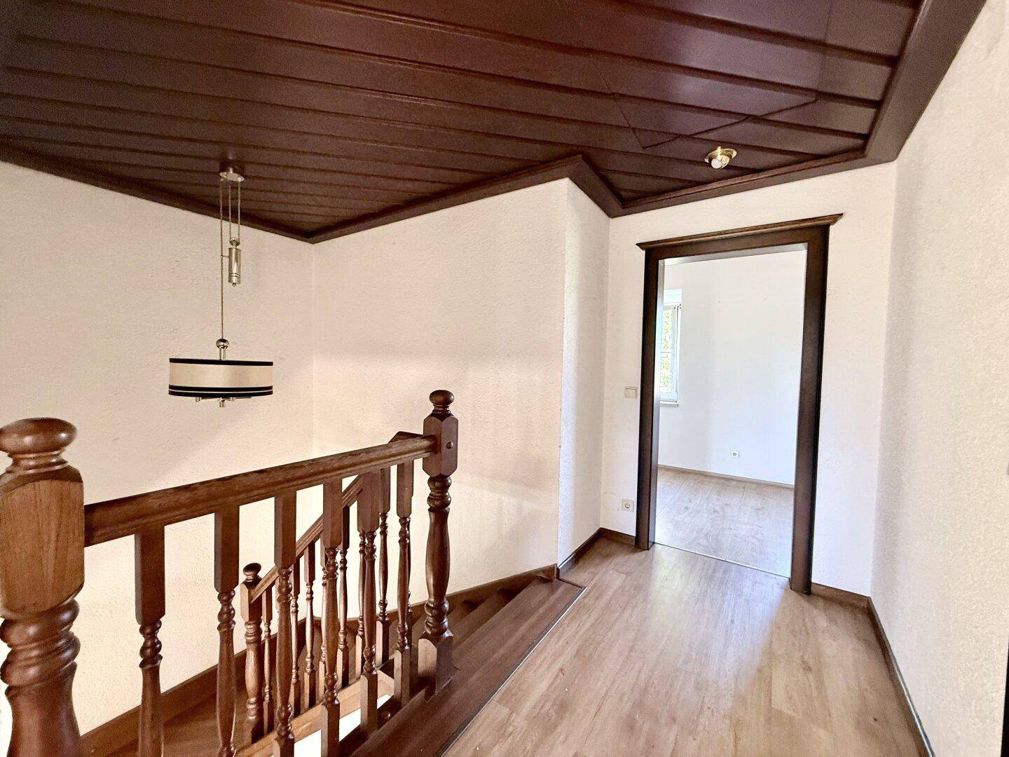 Treppenhaus mit Holzgeländer und dunkler Holzdecke, das die oberen Etagen des Hauses verbindet.