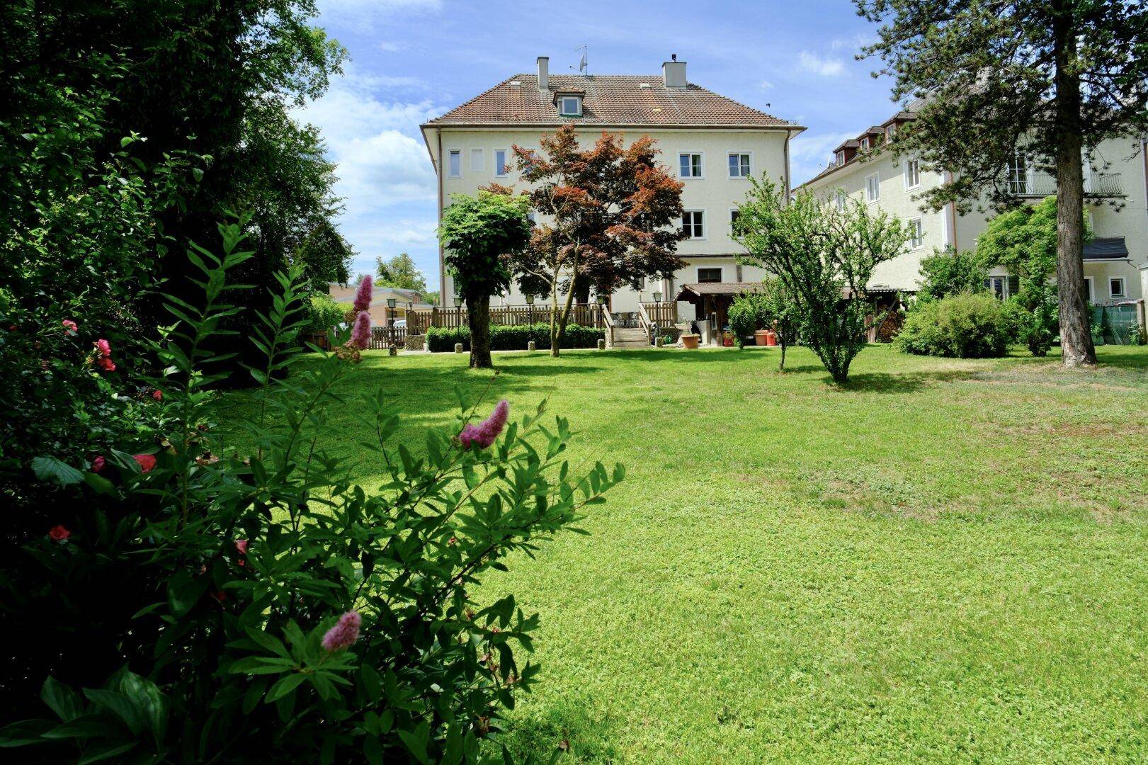 Großzügiger Gartenbereich mit Rasenfläche und Blick auf das Mehrfamilienhaus.