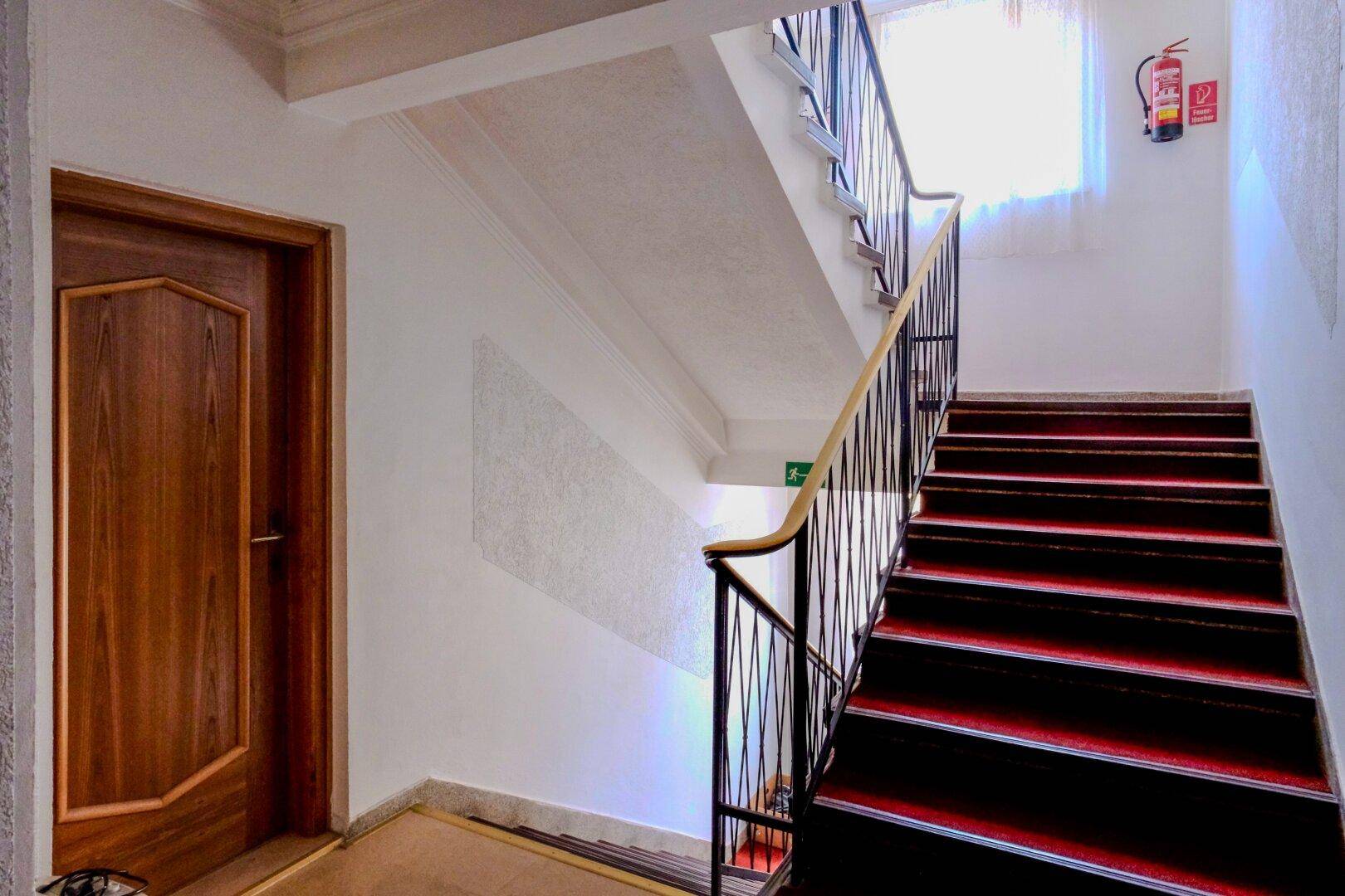Treppenhaus mit rotem Teppich, Holzgeländer und einem Fenster für natürliches Licht.