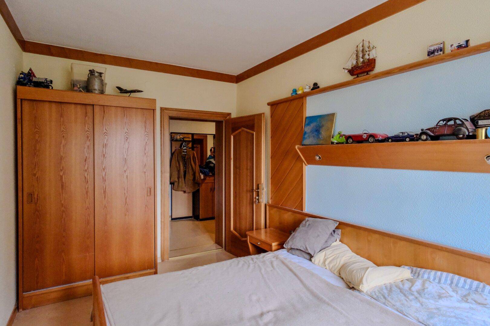 Schlafzimmer mit Holzmöbeln, Doppelbett und dekorativen Regalen an der Wand.