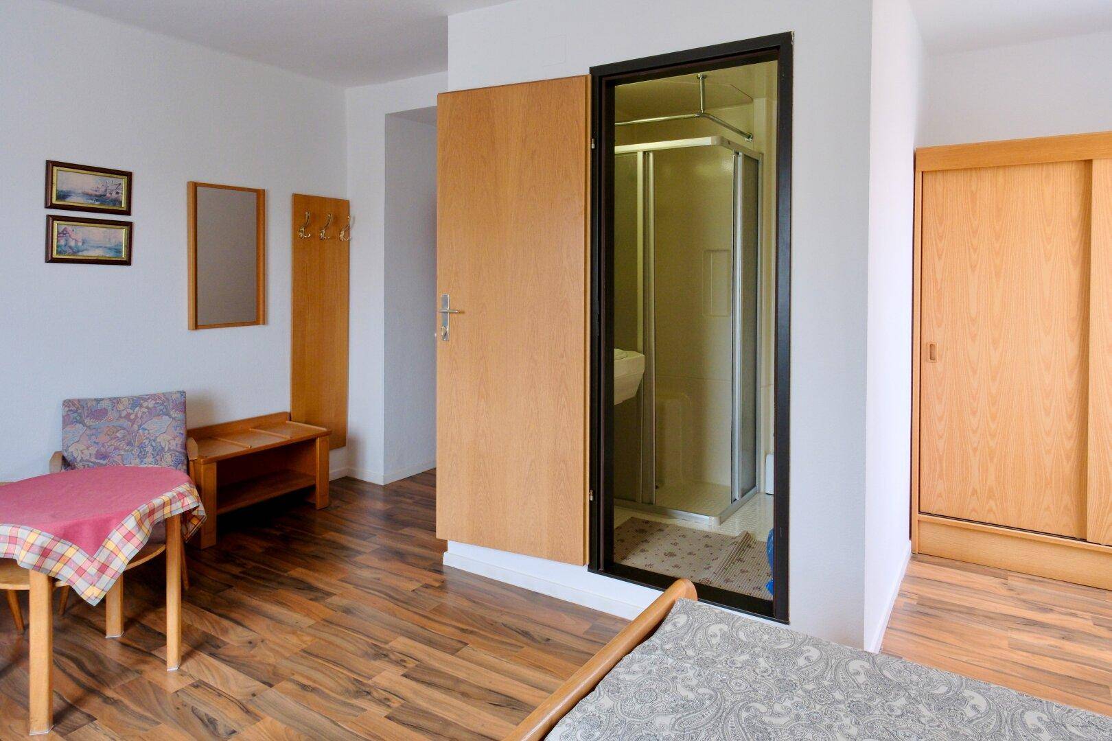 Schlafzimmer mit Holzmöbeln, Doppelbett und einer praktischen Duschkabine im Raum.