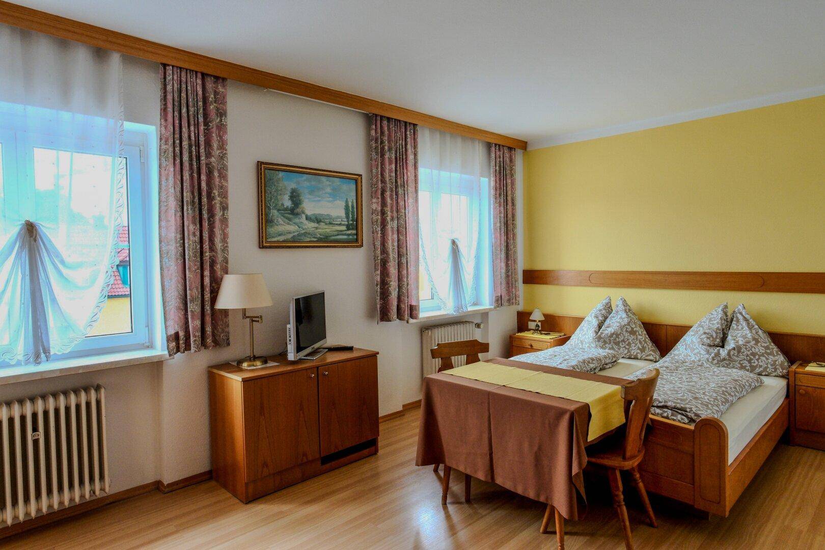 Gemütliches Schlafzimmer mit zwei Einzelbetten, kleinem Esstisch und Fernseher.