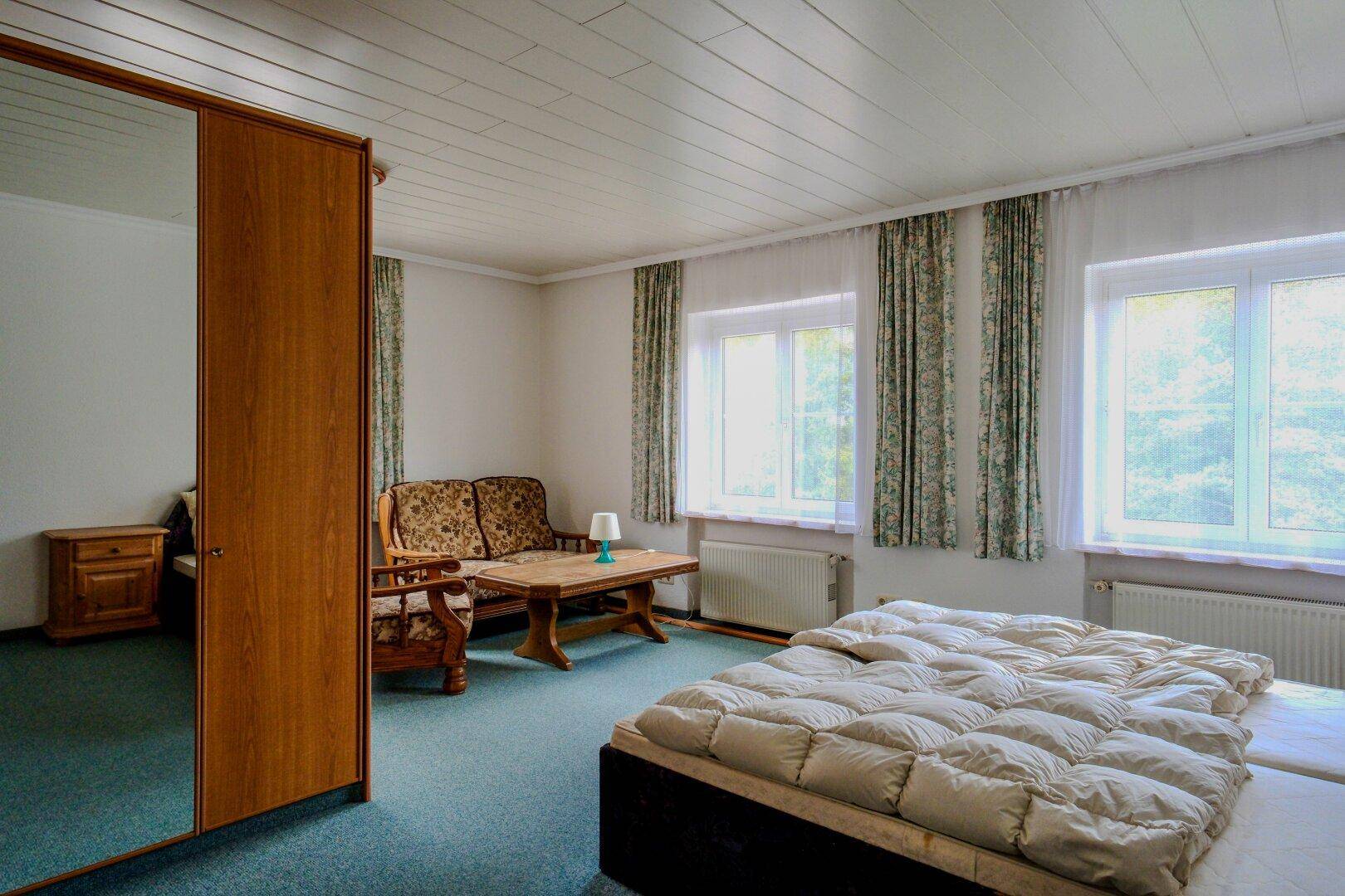 Geräumiges Schlafzimmer mit zwei Betten, Sofa und grünem Teppichboden.