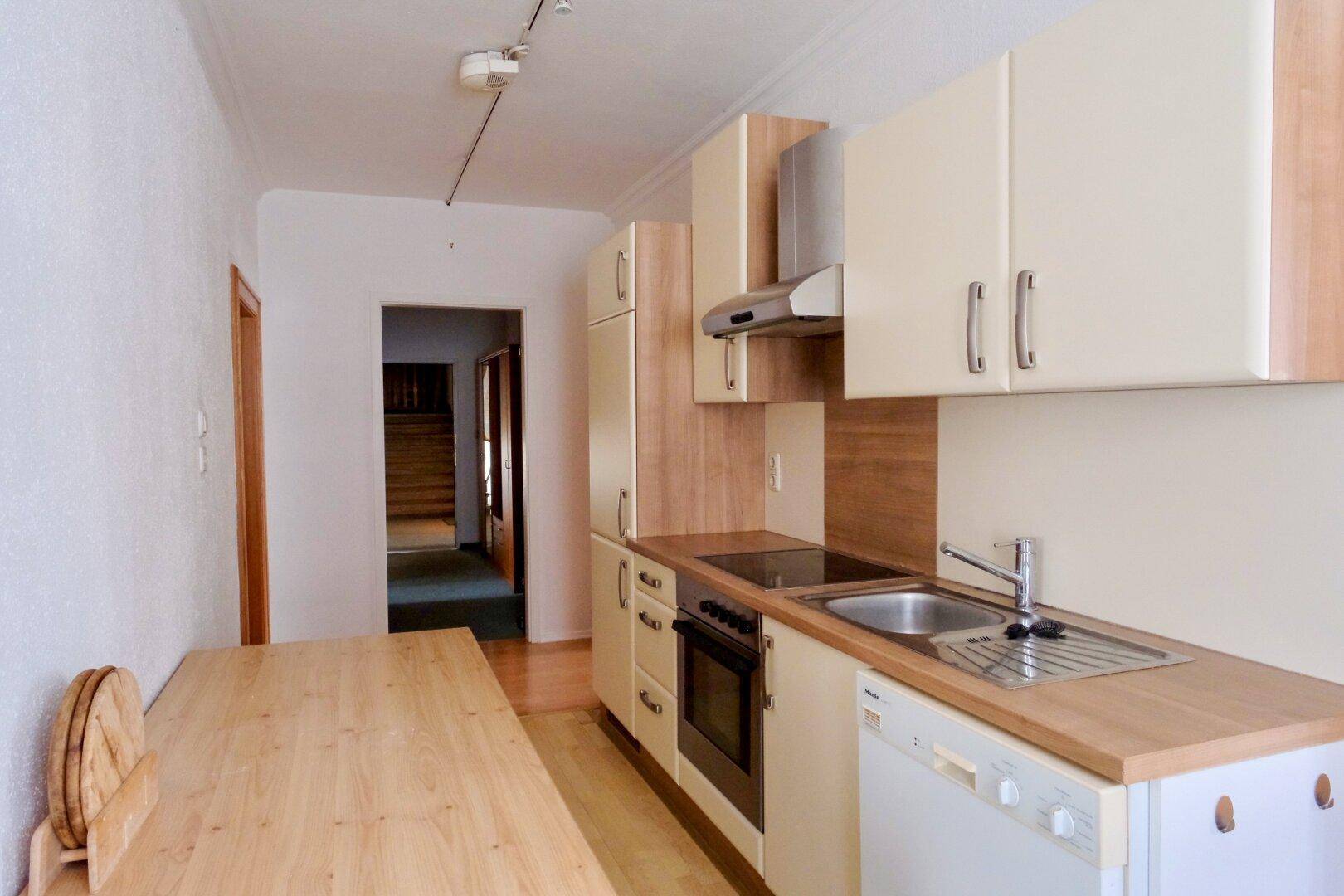 Kleine Küche mit hellen Einbauschränken, Holztheke und Esstisch.