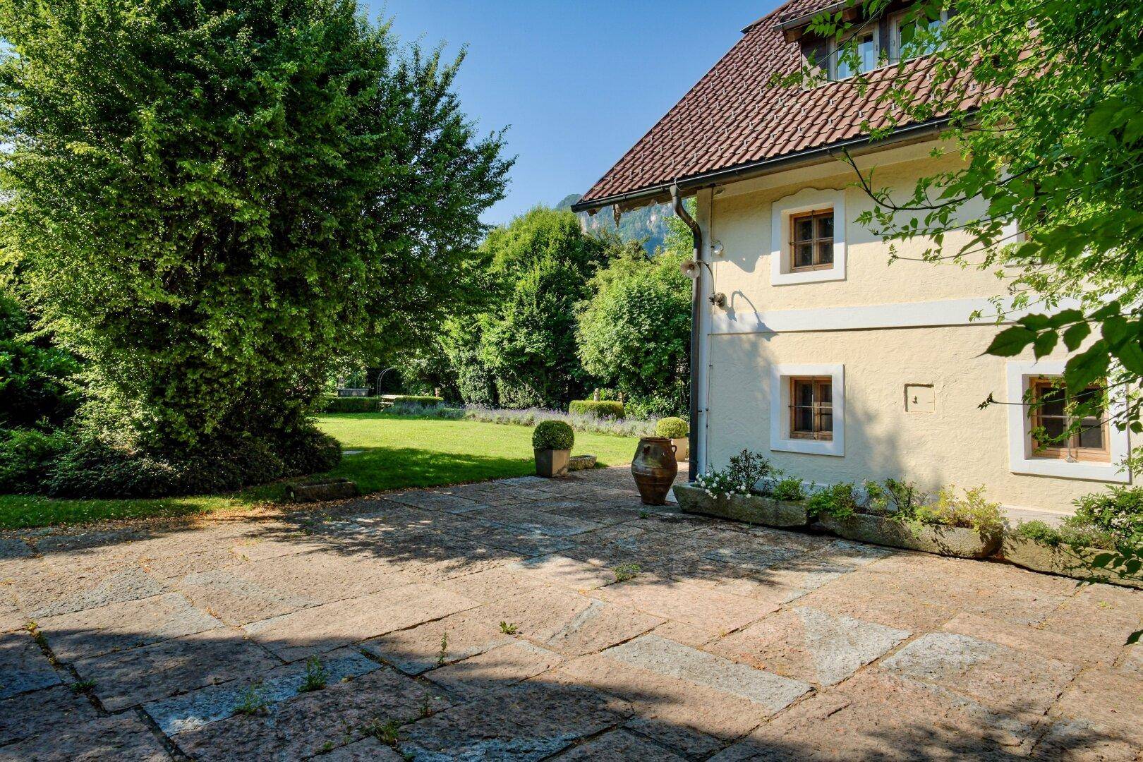 Gedeckte Terrasse mit Natursteinplatten und Blick auf den weitläufigen Garten und die umliegende Natur.
