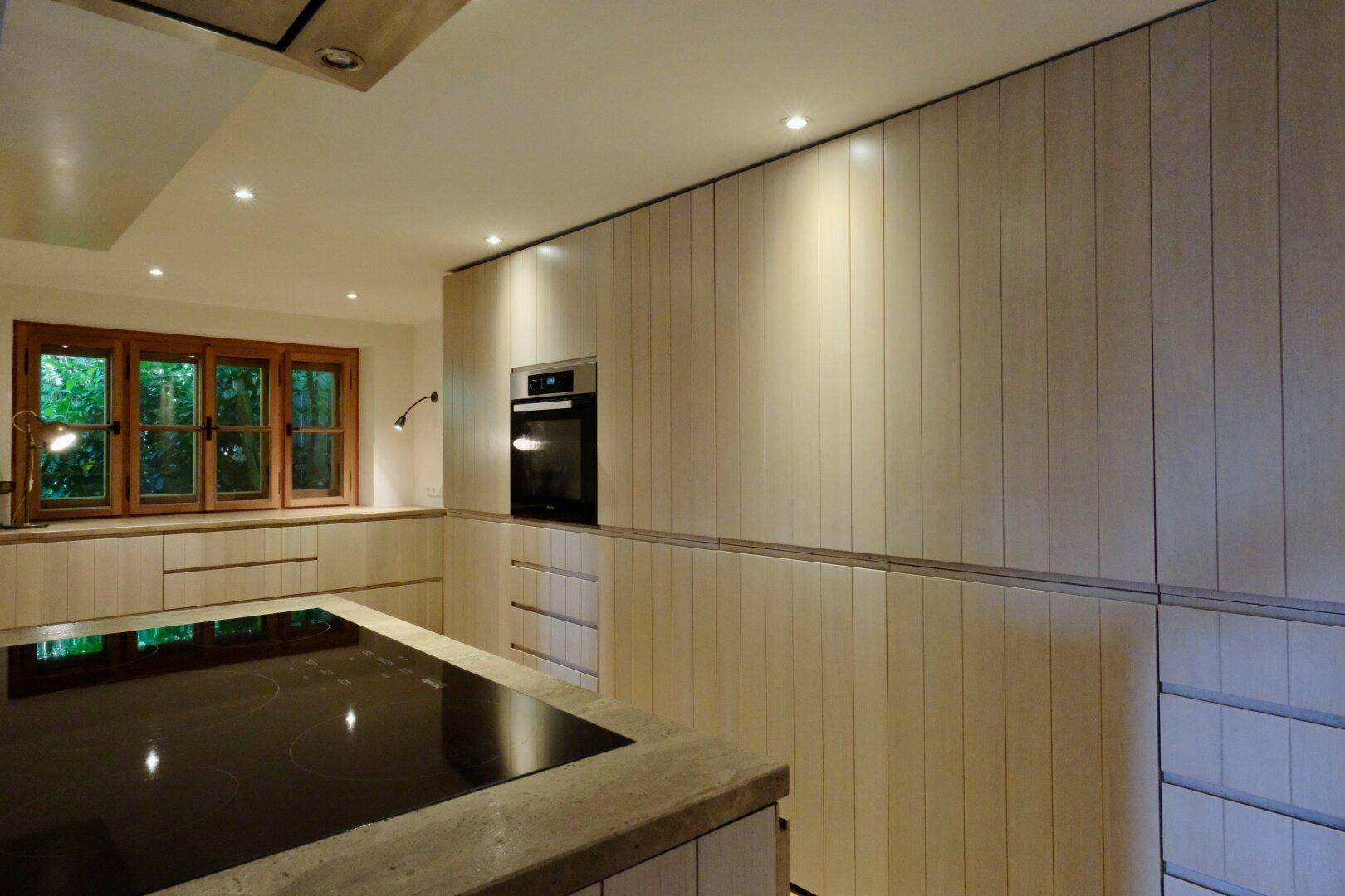 Moderne Einbauküche mit hellen Holzfronten, integriertem Backofen und Kochinsel mit Induktionskochfeld.