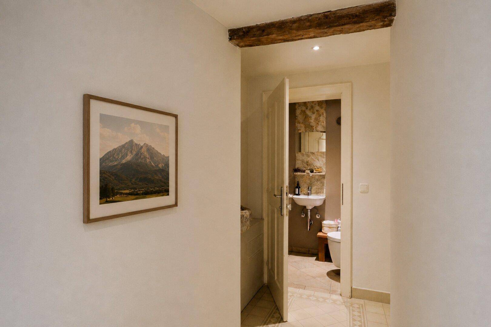 Flur mit Bergbild an der Wand, der zu einem kleinen Gäste-WC mit Waschbecken und Toilette führt.