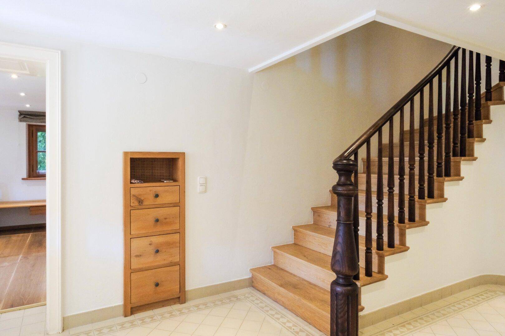 Heller Flur mit Holztreppe und Geländer, kombiniert mit Fliesenboden und einer Holzkredenz.