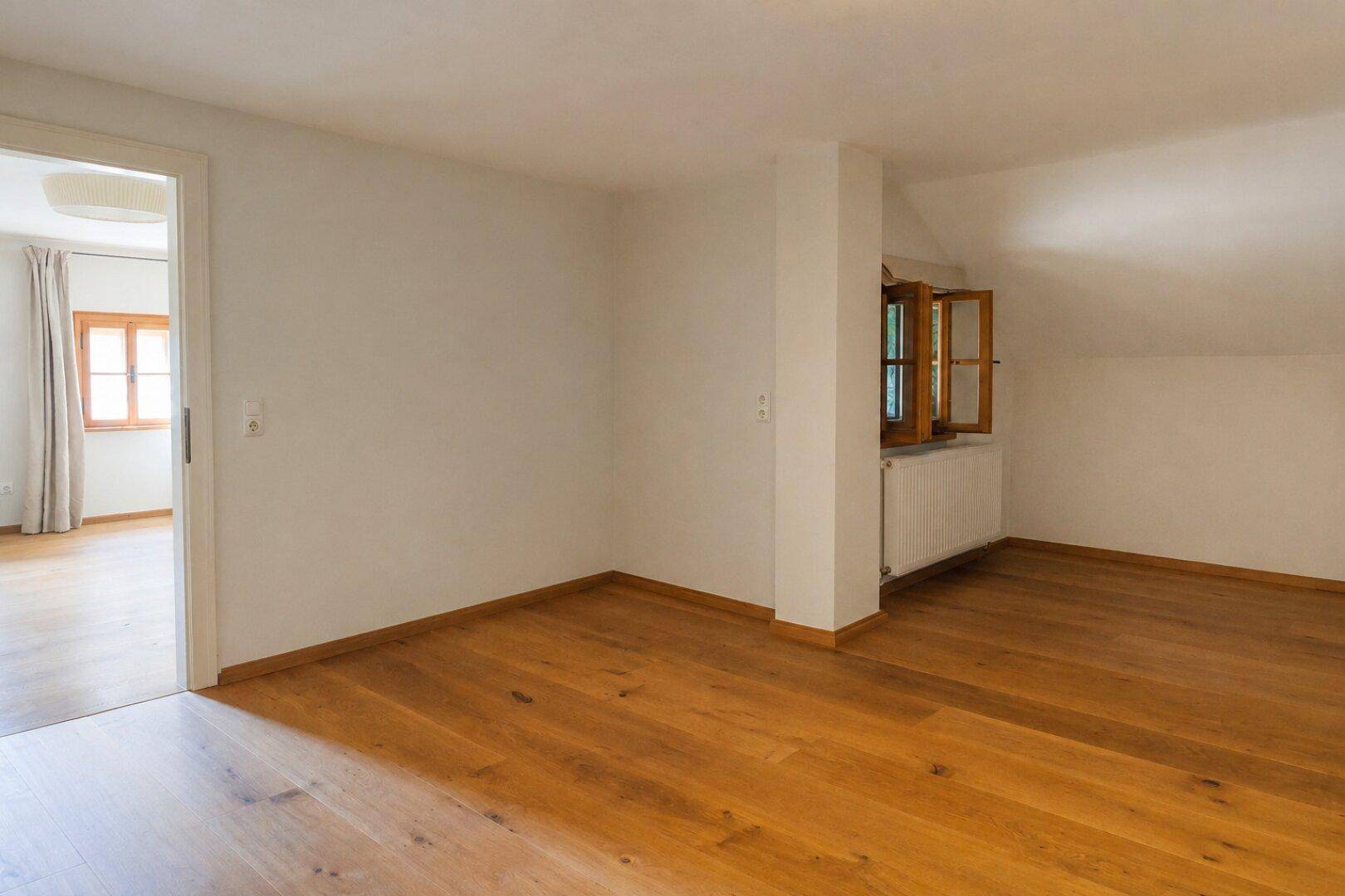Helles Schlafzimmer mit Holzboden, Dachschräge und Fenster mit Blick ins Grüne.