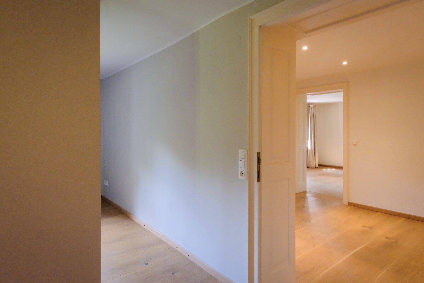 Heller Flur mit Holzboden und offener Tür, die den Blick in einen weiteren Raum freigibt.