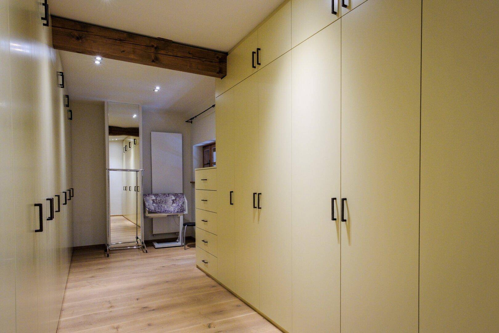 Geräumiger begehbarer Kleiderschrank mit hellen Einbauschränken und Holzboden.