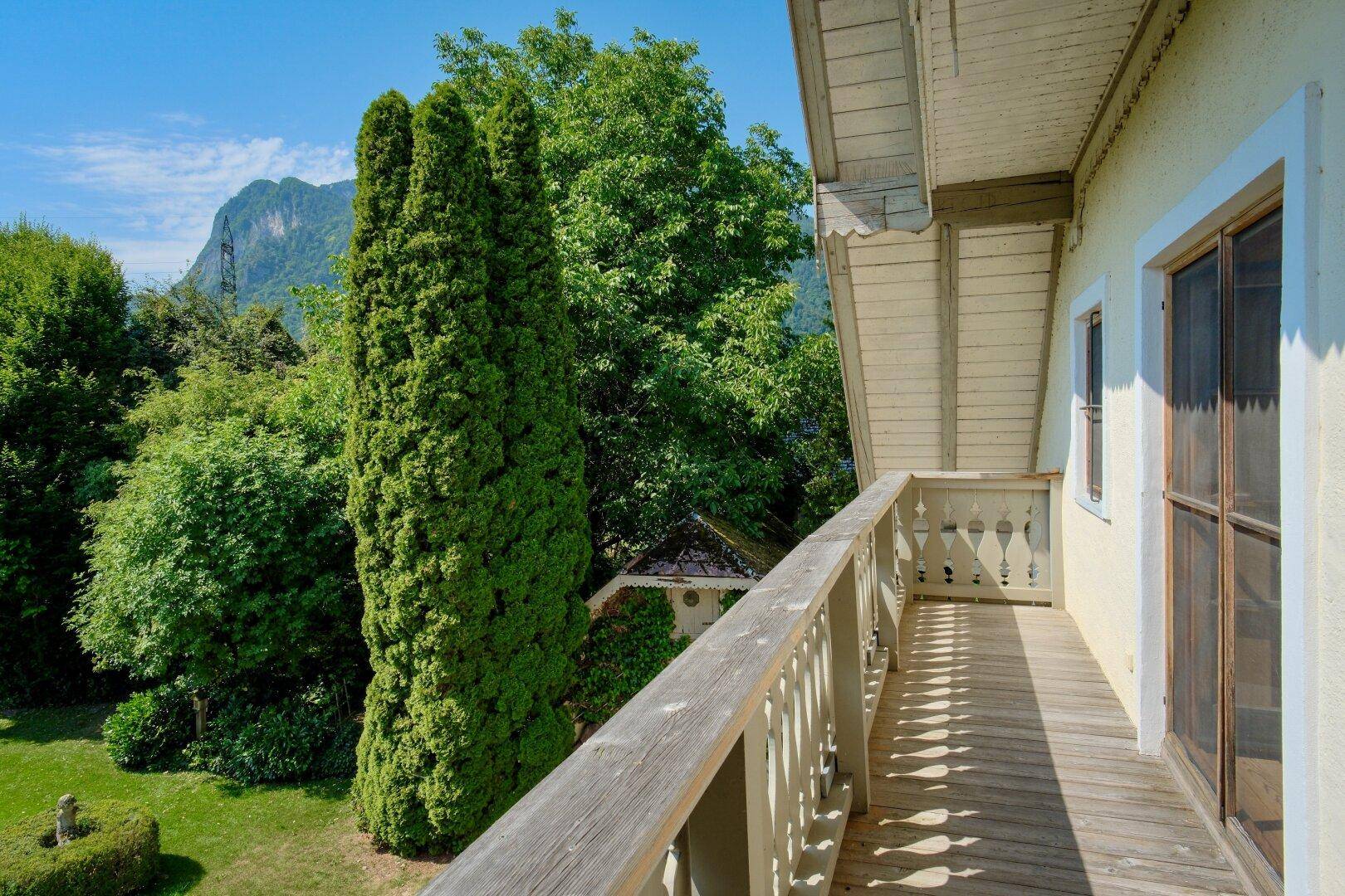 Traditioneller Holzbalkon mit Geländer und Blick auf die grüne Umgebung und einen Berg.