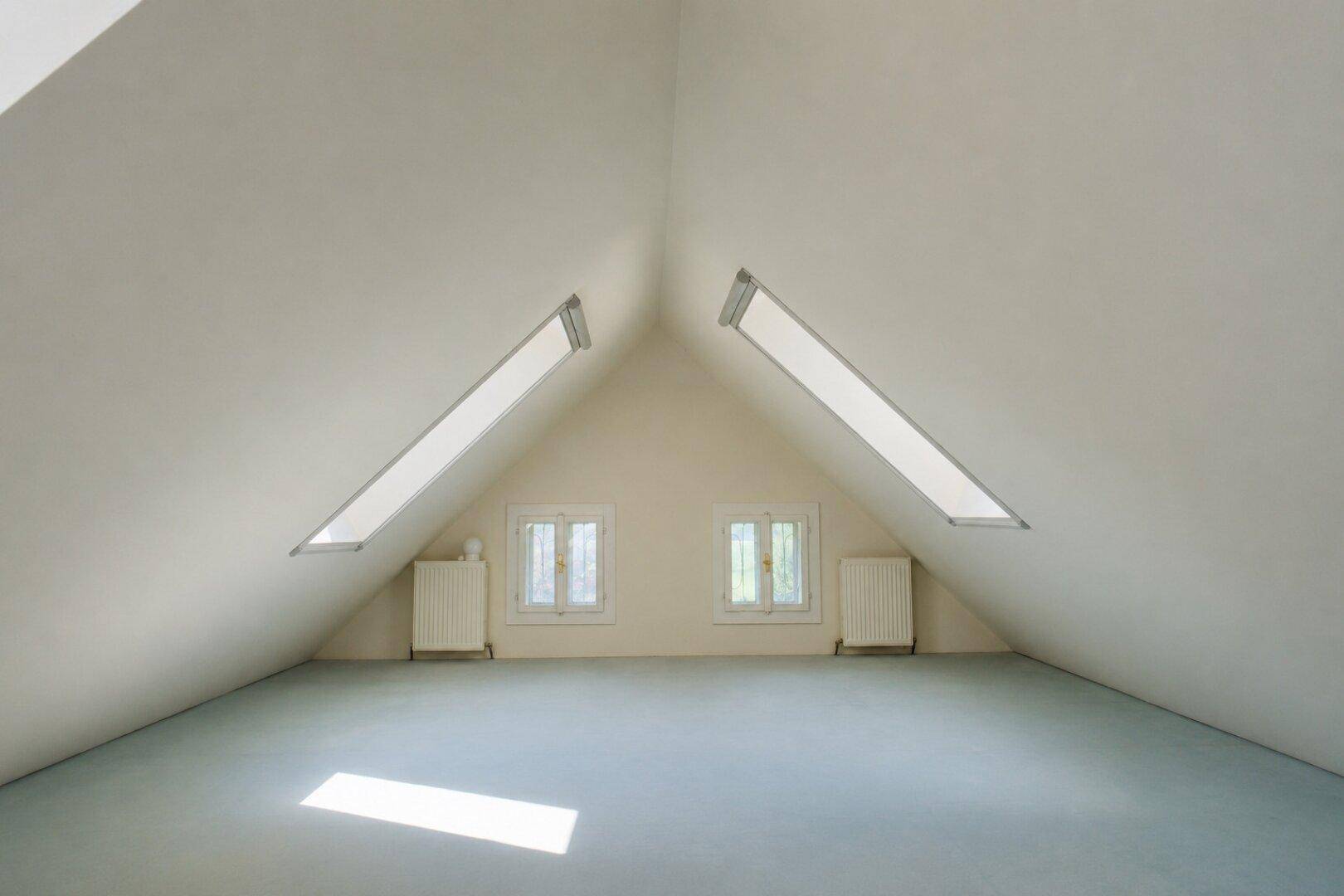 Heller Dachbodenraum mit Teppichboden, Dachschrägen und zwei Dachfenstern für natürliches Licht.