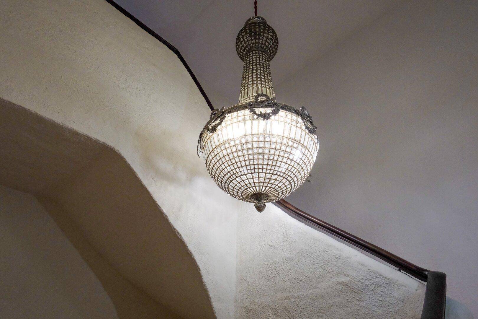 Opulenter Kronleuchter in einem eleganten Treppenhaus mit gewölbten Wänden, der eine klassische Atmosphäre schafft.