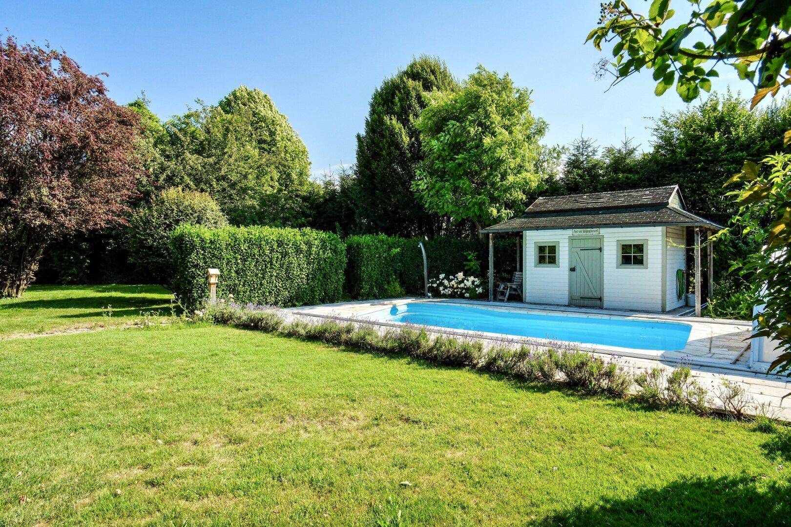 Großer Gartenbereich mit Schwimmbad und einem charmanten Poolhaus, umgeben von üppigem Grün und Bergen.