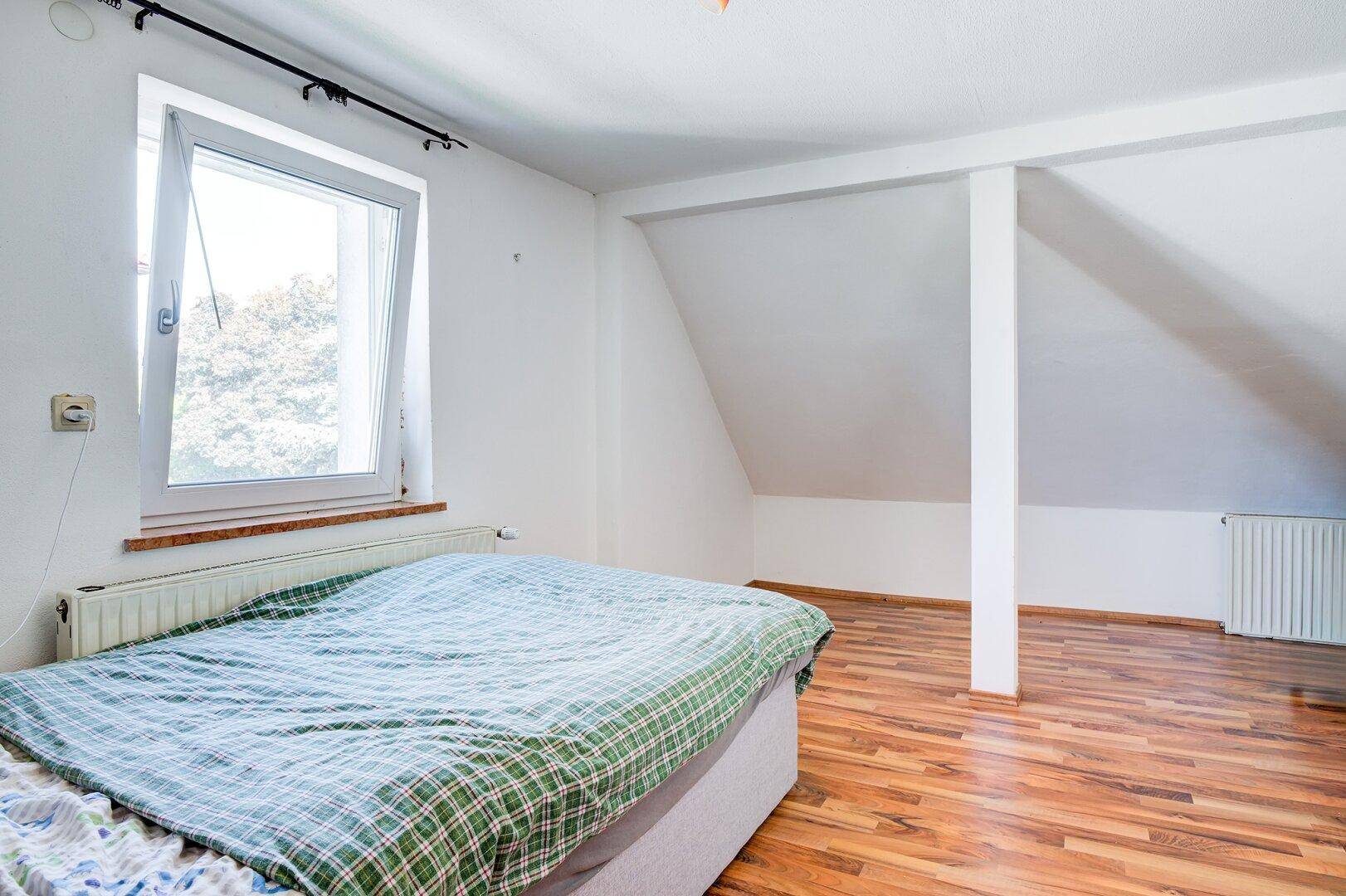 Helles Schlafzimmer im Dachgeschoss mit Holzfußboden und Dachschräge.