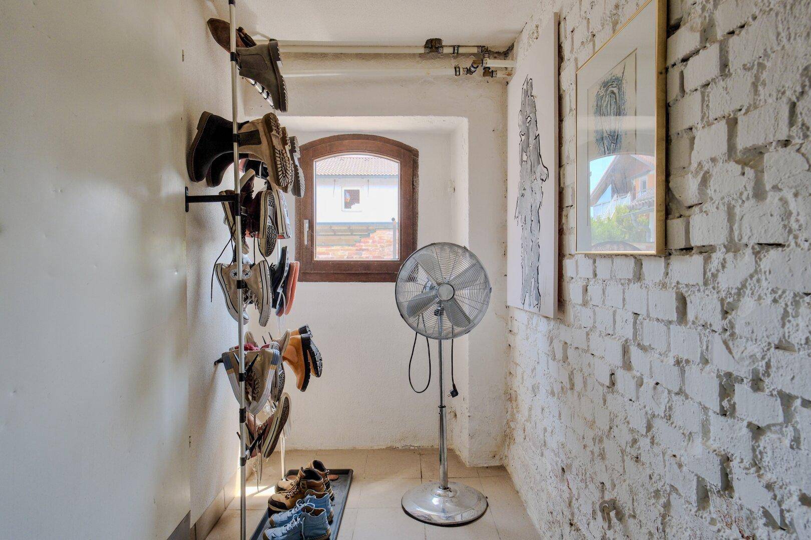 Schmaler Flur mit weiß gestrichenen Ziegelwänden, Schuhregal und einem Fenster.