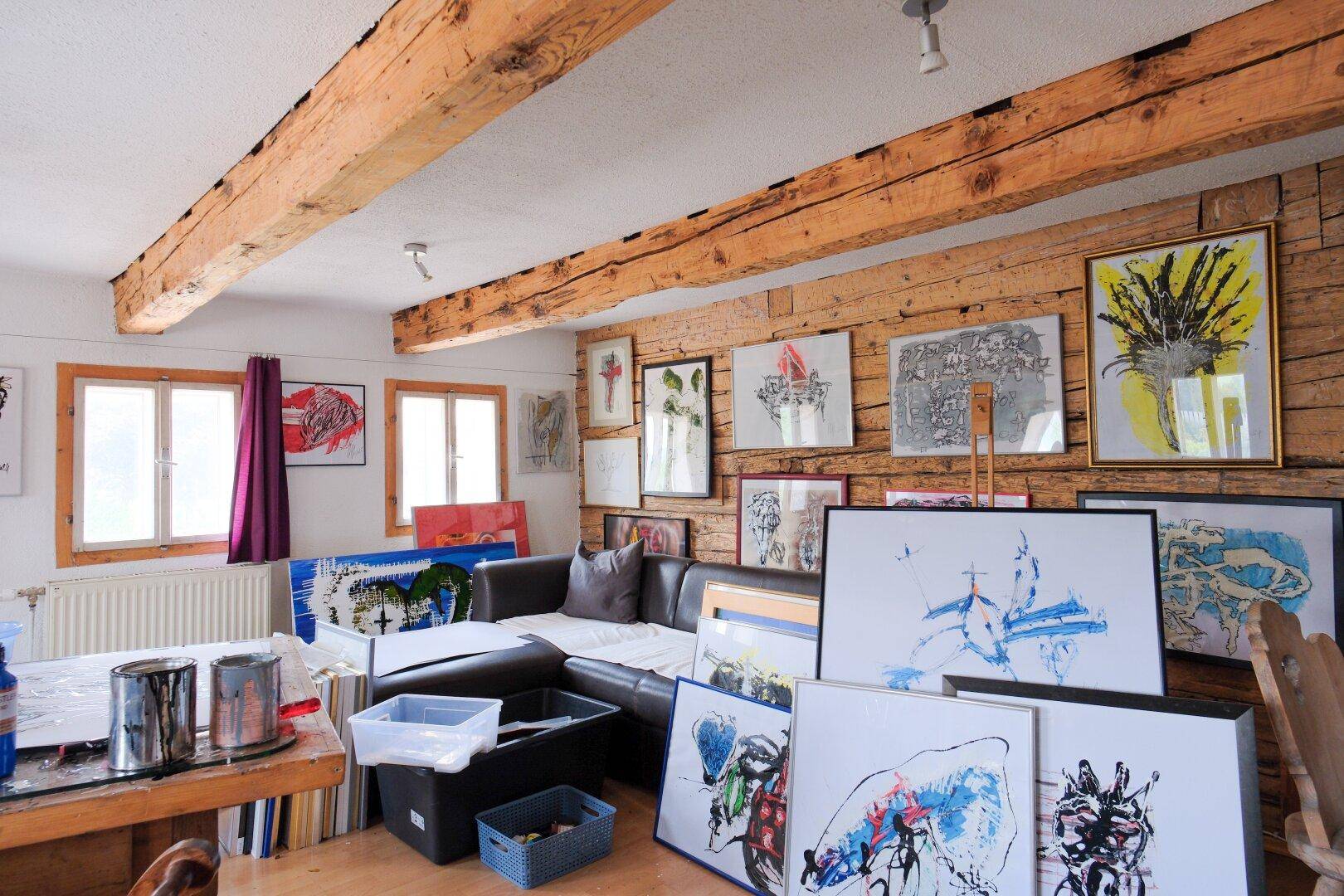 Kreatives Atelier mit Holzbalkendecke, Kunstwerken und einem Sofa.