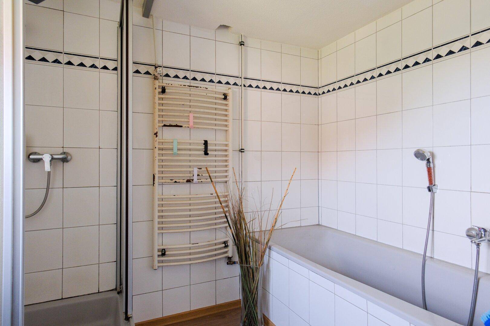 Helles Badezimmer mit Badewanne, Duschkabine und beheiztem Handtuchhalter.