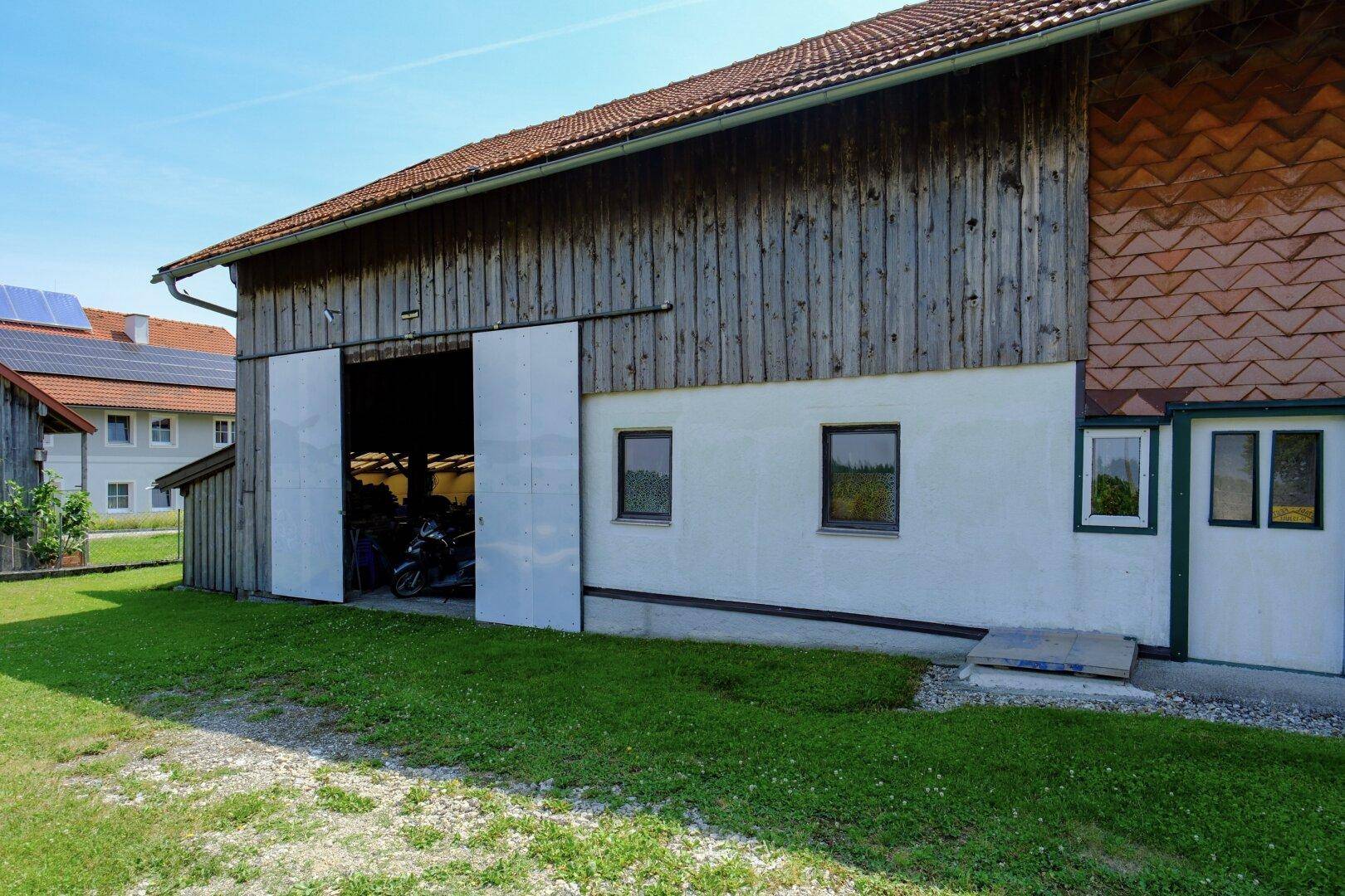 Scheunentor eines Nebengebäudes mit Grasfläche und Zufahrt.