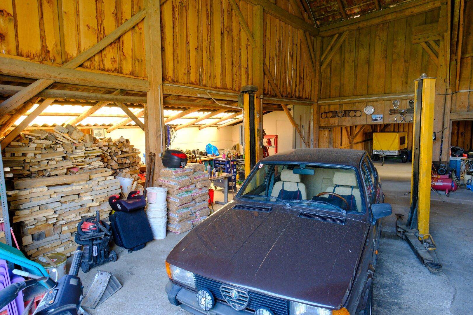 Geräumige Garage mit Hebebühne, Werkzeugen und gelagertem Holz.