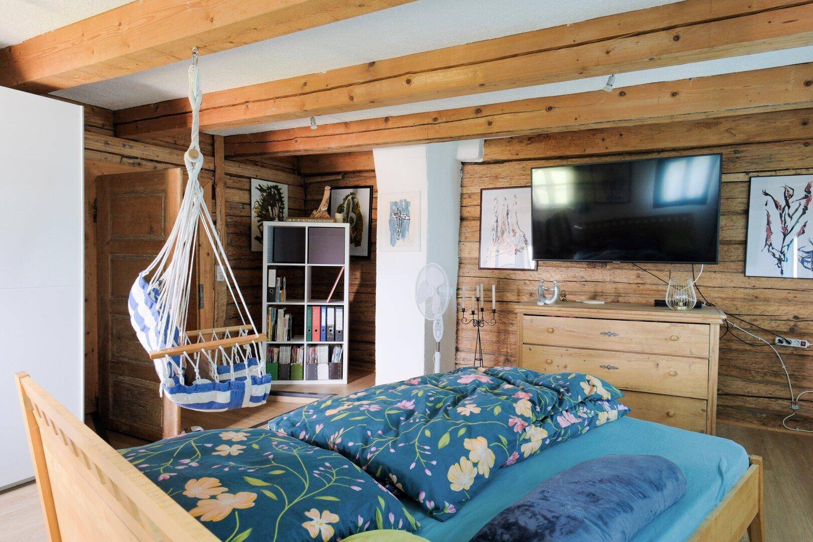 Gemütliches Schlafzimmer mit Holzbalkendecke, Holzwänden und einem Hängesessel.