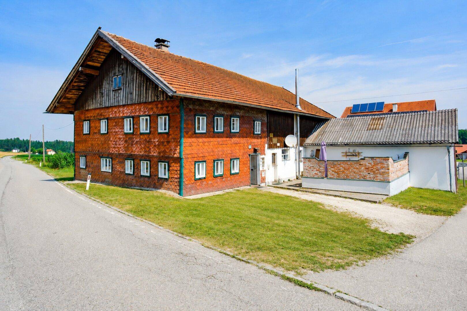 Traditionelles Bauernhaus mit rotem Ziegeldach und Holzfassade in ländlicher Umgebung.