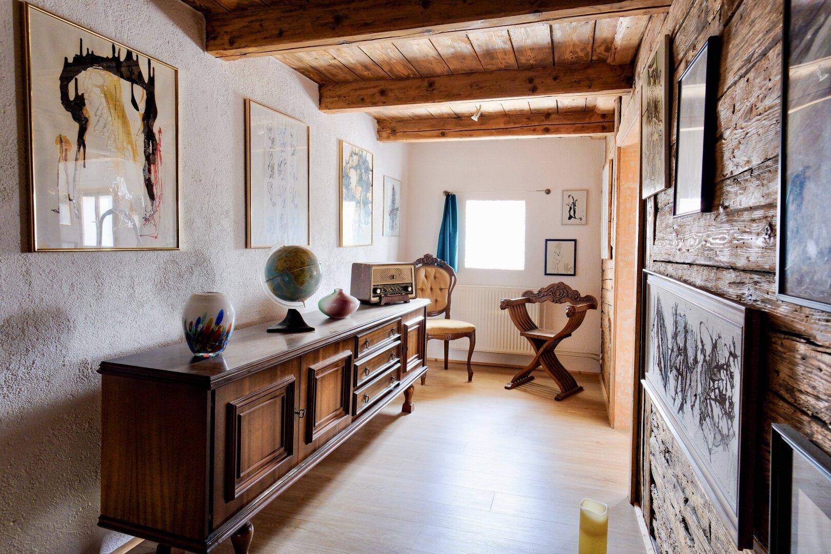 Geräumiger Flur mit antiker Kommode, Holzbalkendecke und Kunstwerken an den Wänden.