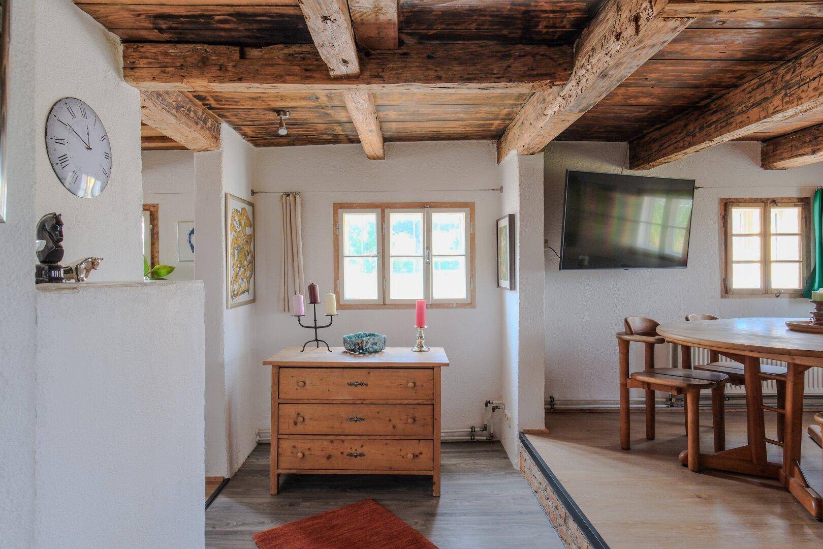 Rustikaler Übergangsbereich mit Holzbalkendecke, Kommode und Blick auf den Essbereich.