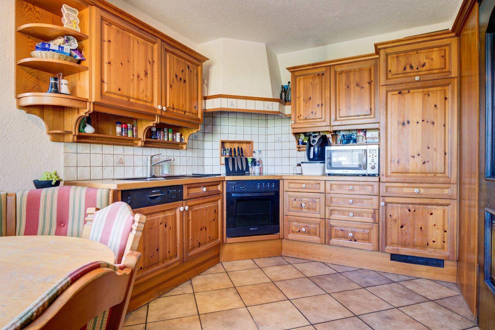 Traditionelle Holzküche mit Einbauschränken, Fliesenboden und Essbereich, funktional und einladend.