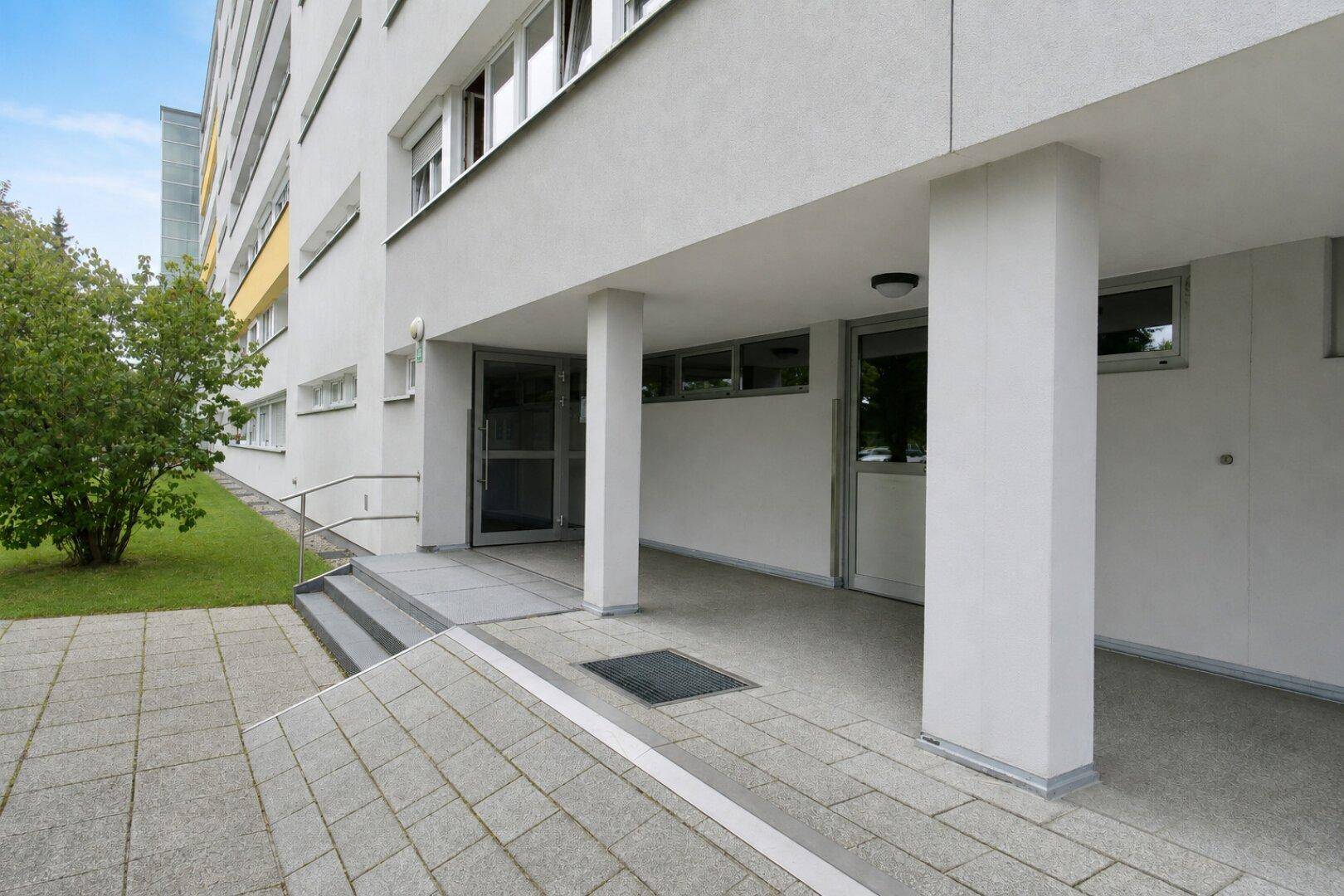 Eingangsbereich eines Mehrfamilienhauses mit Rampe und Säulen.