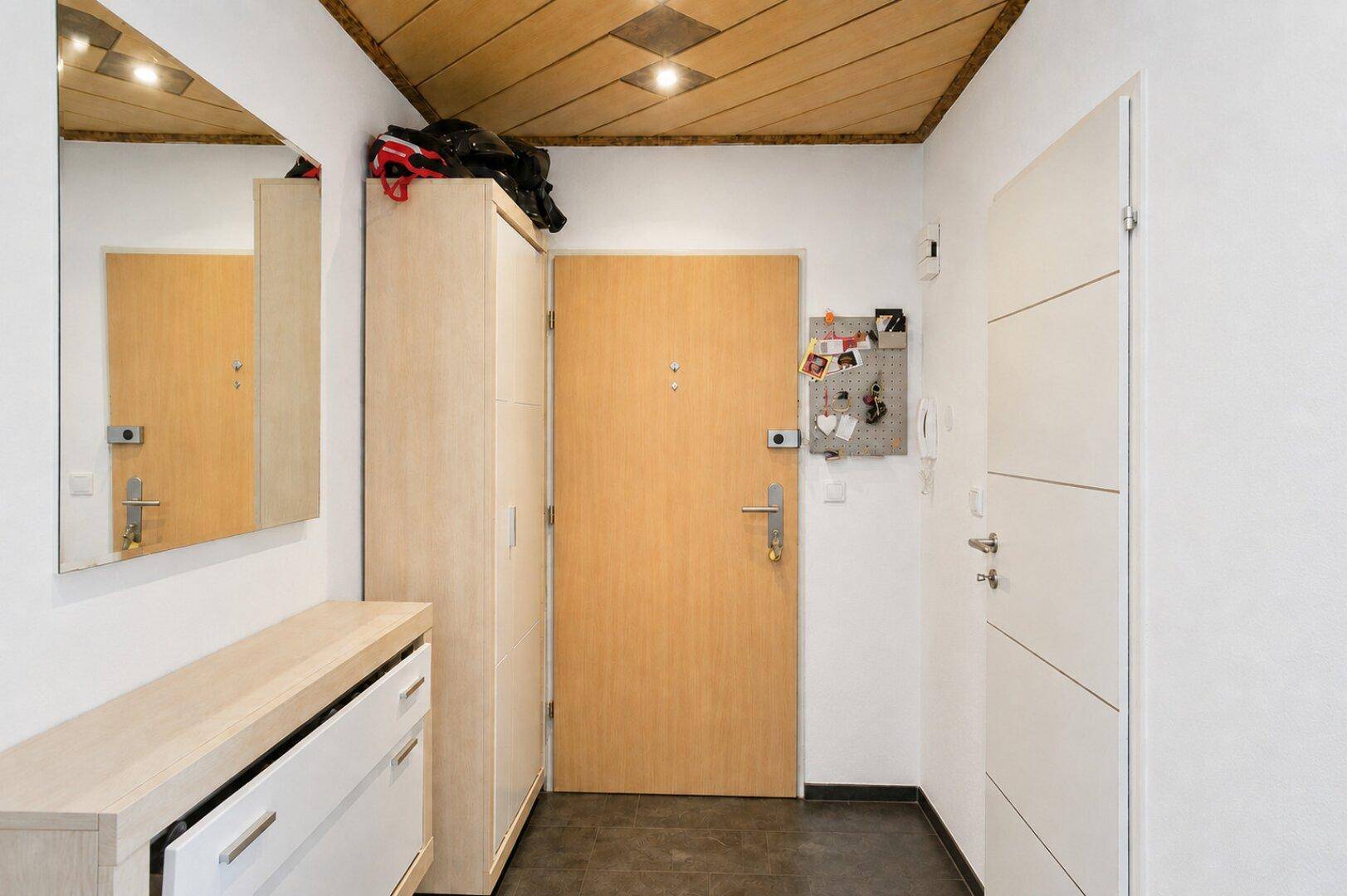 Heller Eingangsbereich mit Holzdecke, Spiegel und praktischen Möbeln.