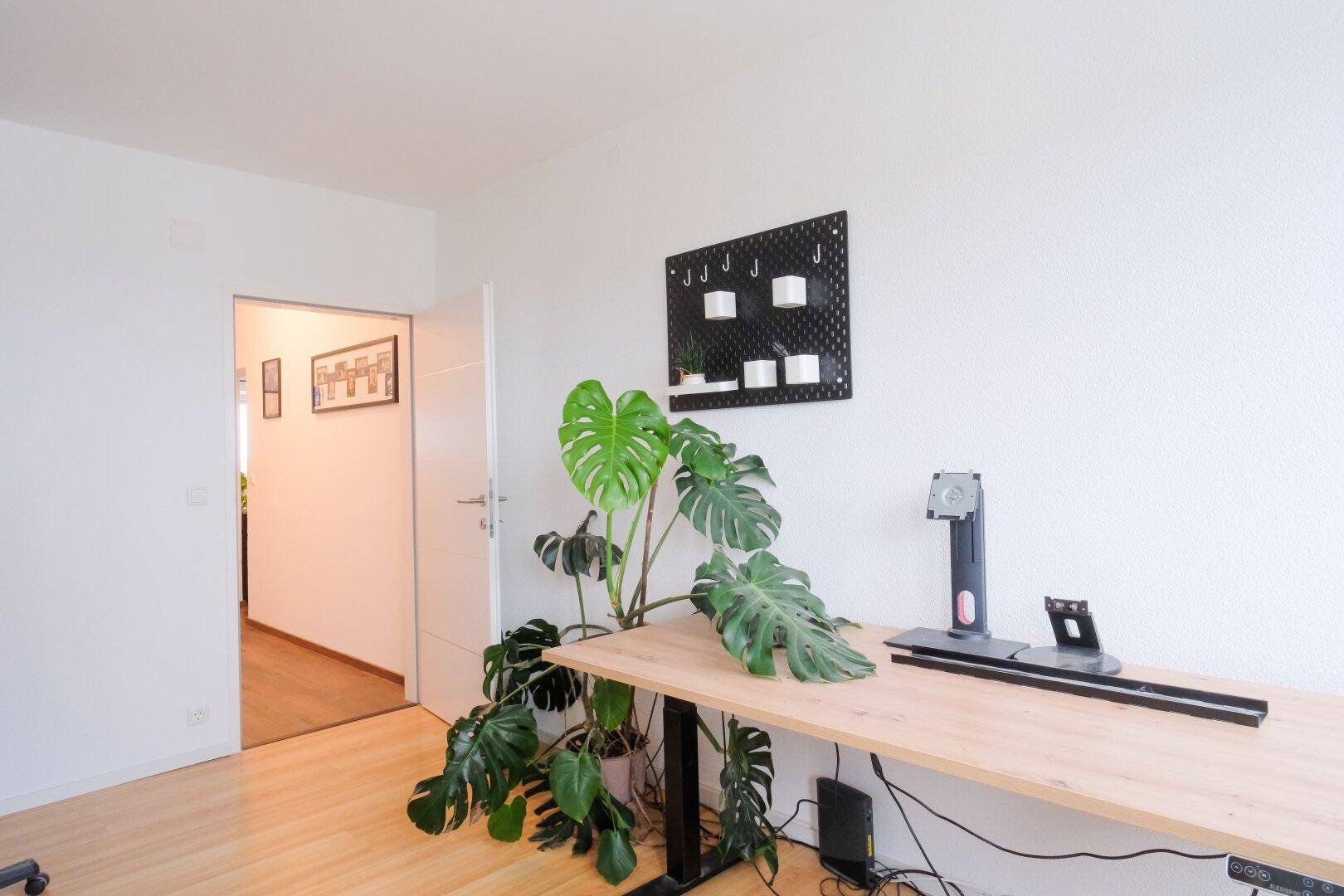 Modernes Arbeitszimmer mit Holzschreibtisch, großer Pflanze und hellem Holzboden.