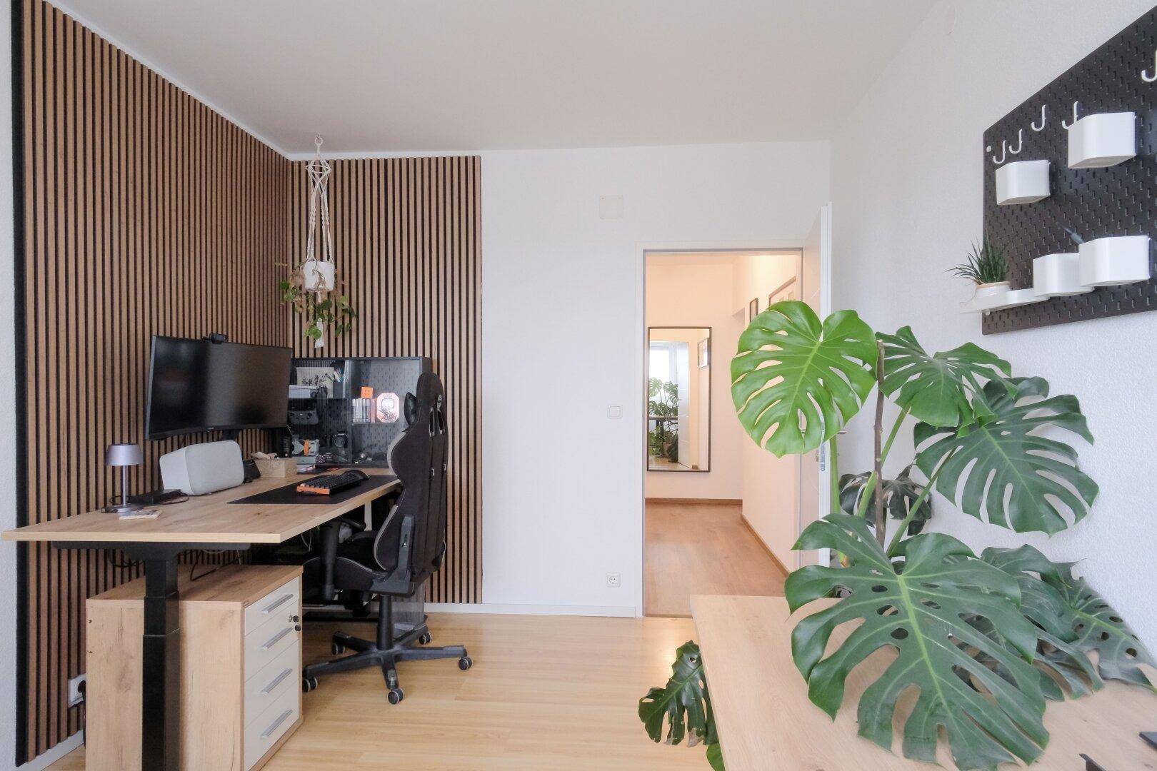 Modernes Arbeitszimmer mit Holzlamellenwand, Schreibtisch und hellem Holzboden.