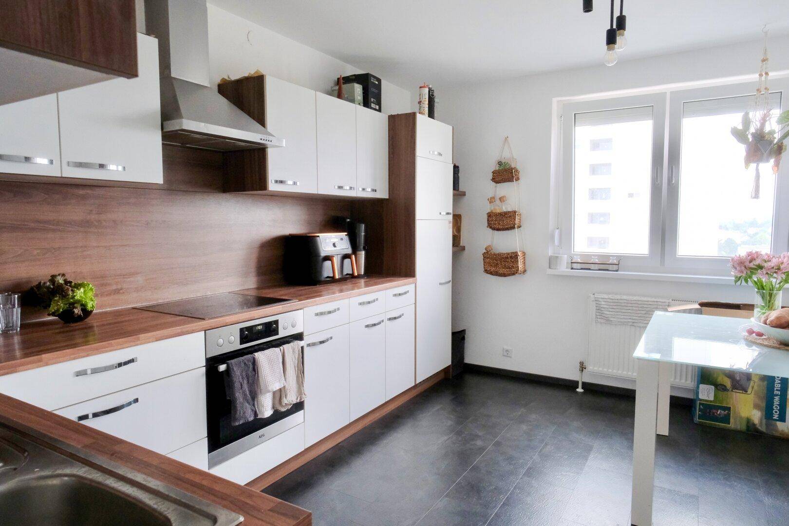 Moderne Küche mit weißen Schränken, Holzarbeitsplatten und dunklem Fliesenboden.