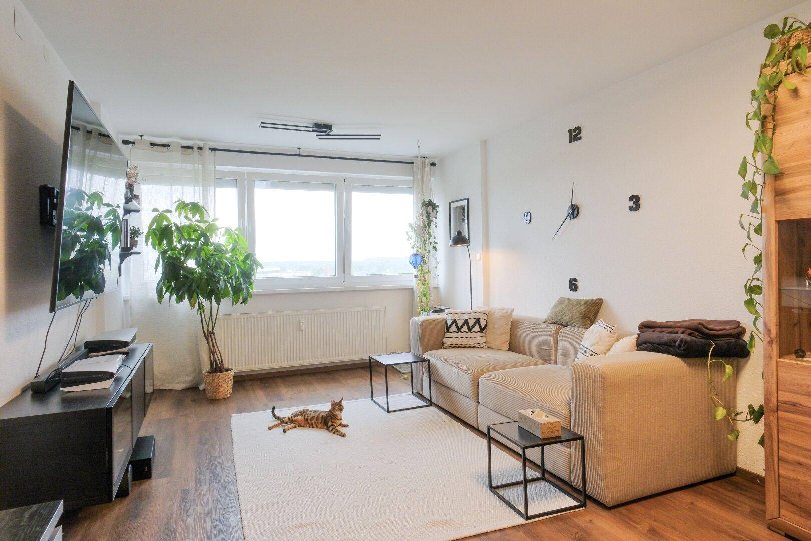 Helles Wohnzimmer mit großem Sofa, Fernseher und Blick ins Grüne.