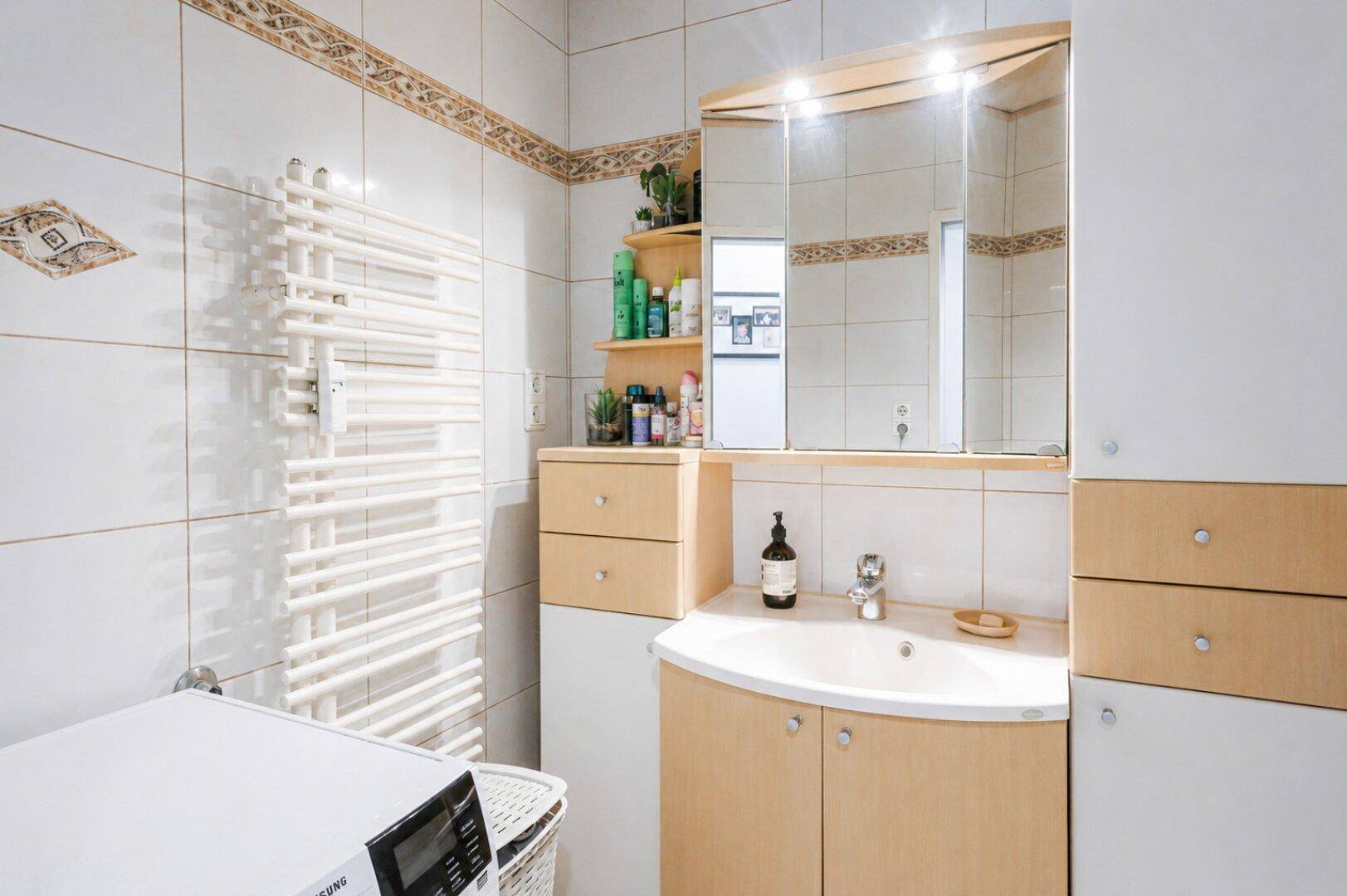 Badezimmer mit Waschbecken, Spiegelschrank, Handtuchheizkörper und Fliesen.