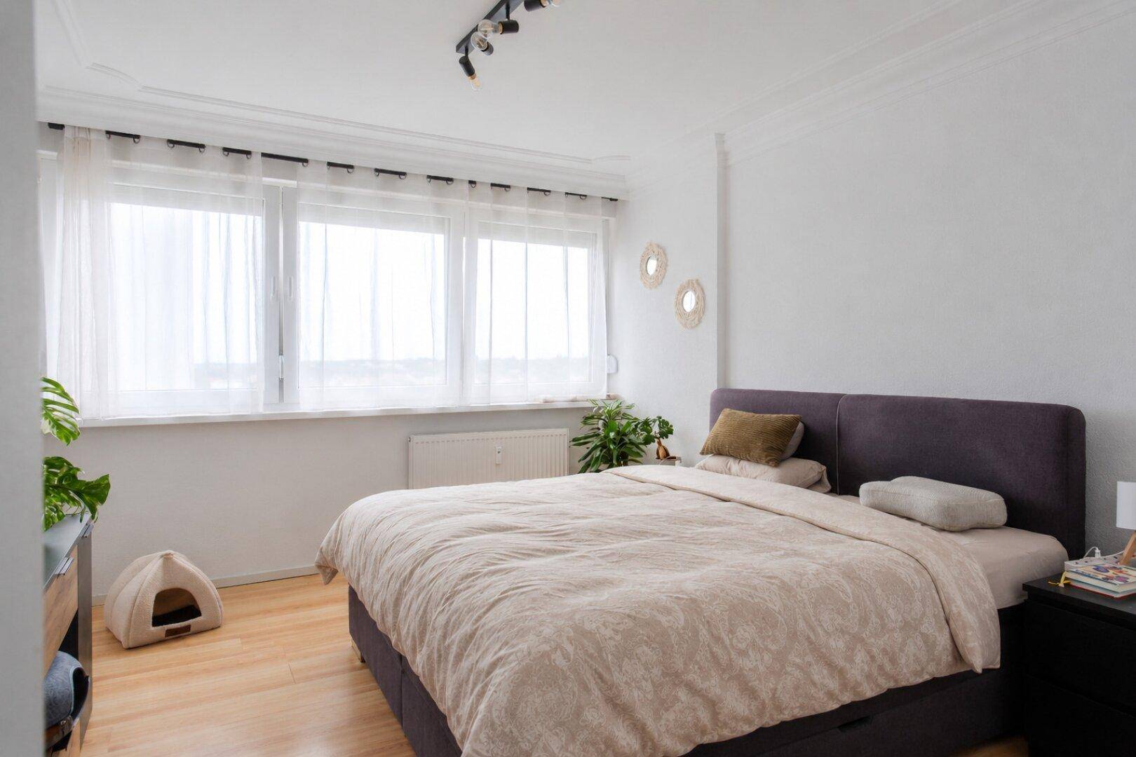 Helles Schlafzimmer mit Doppelbett, Holzboden und großen Fenstern.